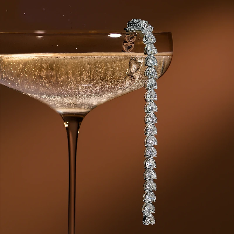 Bracelet with heart-shaped stones hanging from the rim of a champagne coupe
